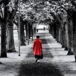 Solitary lady in red coat walking down a dark path