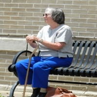 Older lady sitting alone on a bench with a cane.